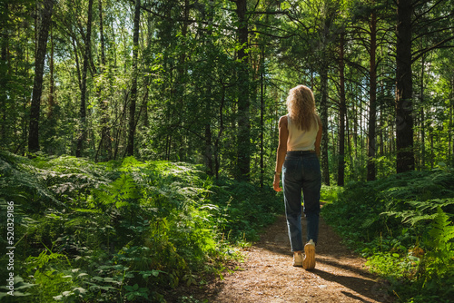 The young woman walks through a dark forest on a sunny day
