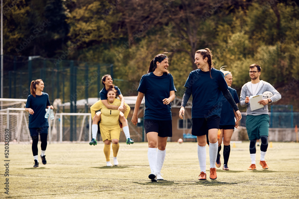 Cheerful female players talk after soccer practice at stadium.