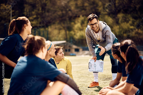Happy coach giving instructions to women s soccer team on playing field.