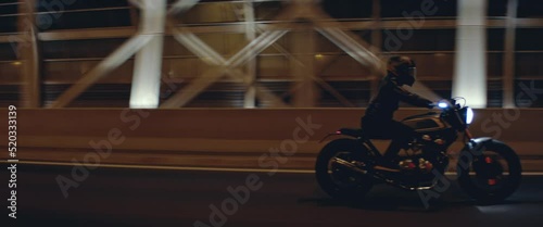 TRACKING Shot of a biker riding his custom built cafe racer motorcycle through city at night. Shot with 2x anamorphic lens photo