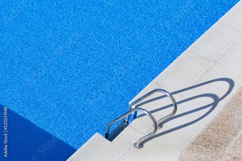 Detalle parcial de una piscina de agua transparente con la escalera de acceso y su sombra en primer plano.