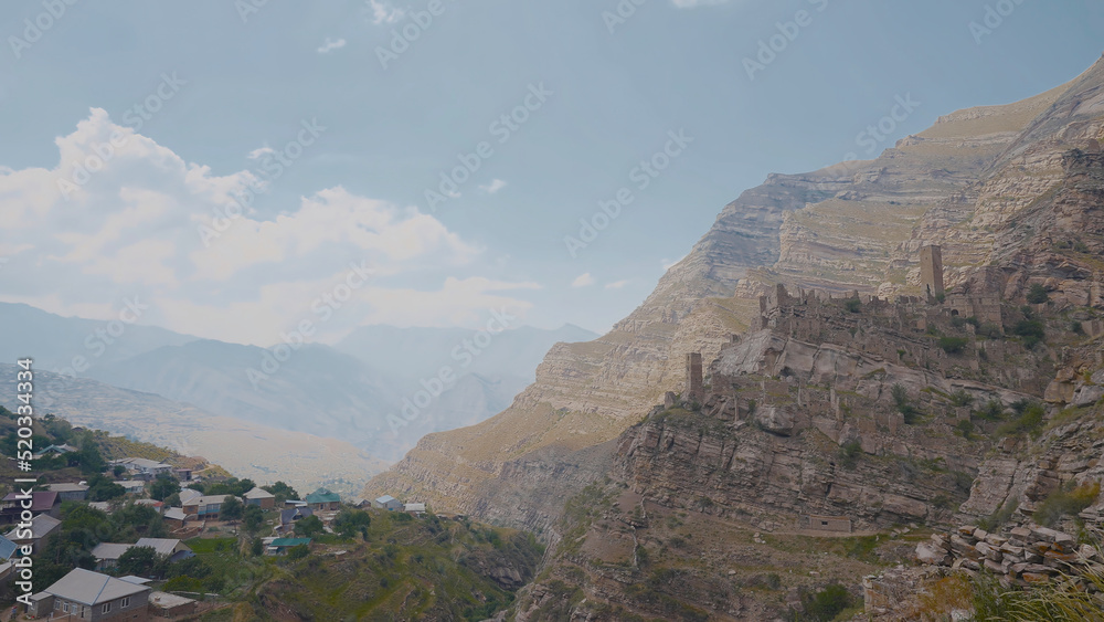 Obraz premium Village near cliff with ruins. Action. Top view of stone city in mountains above residential village. Ancient stone ghost town in mountains