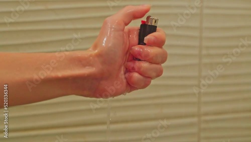 A close-up of a woman's hand tries to light a lighter in the shower under water but she fails. Bad habits. Trying to light a cigarette in the shower.