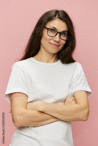 portrait of a cute, attractive brunette in a white tank top on a pink background, with a pleasant smile, standing in glasses for vision