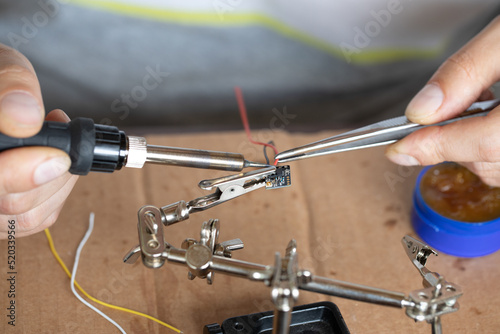 The hand holding the tin, a soldering iron solder the chip in place. a man solders a wire to a microcircuit