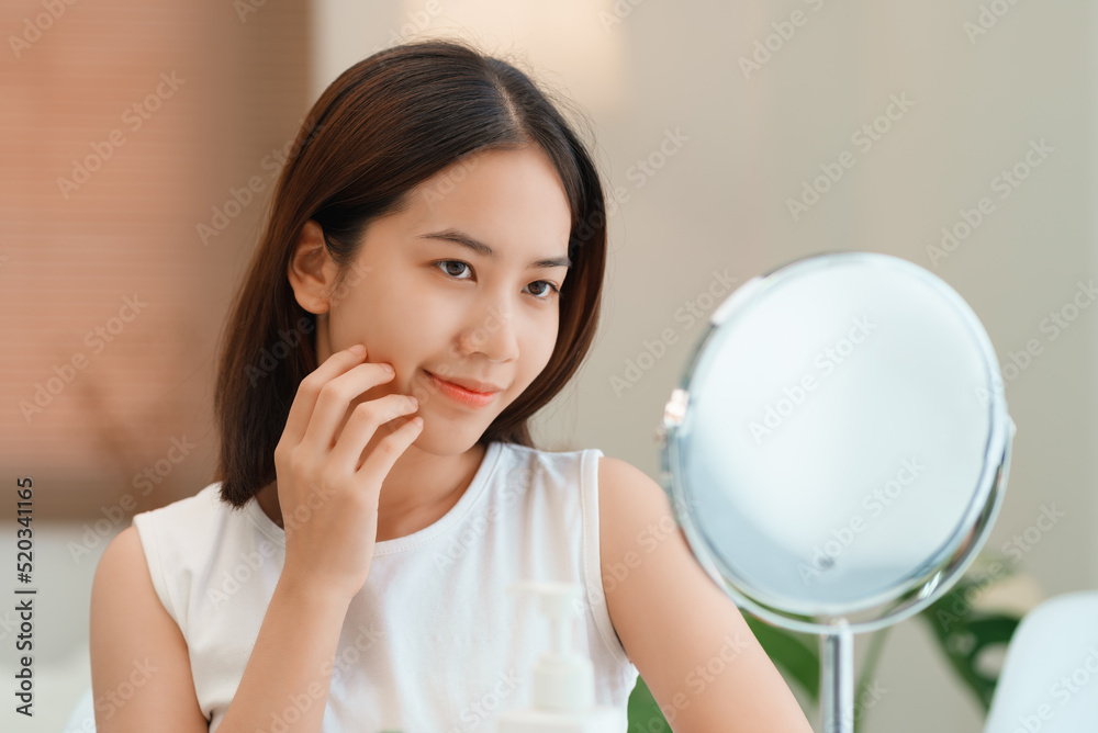 Closeup portrait of smiling young beautiful asian woman looking at mirror touching her skin enjoying treatment for dry skin. Closeup portrait of smiling young beautiful asian woman looking at mirror touching her skin enjoying treatment for dry skin.