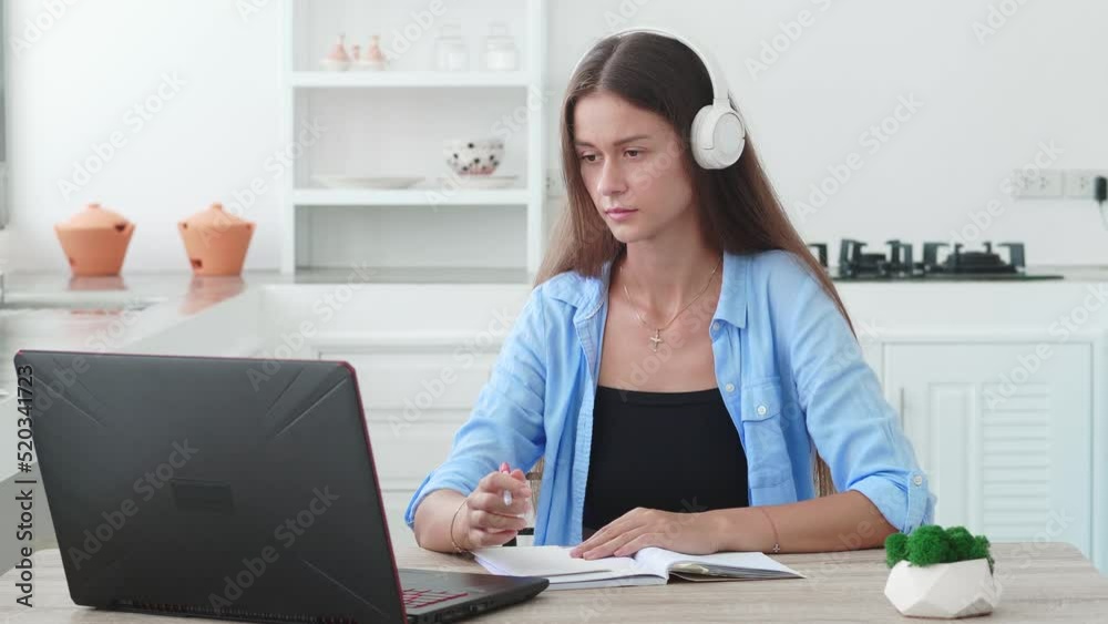 Focused student girl with headphones writing notes at laptop, checking handwriting summary, watching webinar, listening learning audio lecture, taking online virtual training course Focused student girl with headphones writing notes at laptop, checking handwriting summary, watching webinar, listening learning audio lecture, taking online virtual training course