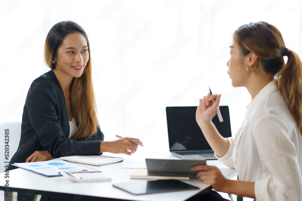Two young Asian businesswomen discuss the concept of a new start-up project. Analyze marketing planning and financial statement at the office. Two young Asian businesswomen discuss the concept of a new start-up project. Analyze marketing planning and financial statement at the office.