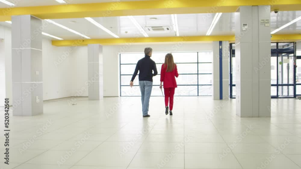 Two businessmen, man and woman, walk through an empty hangar discussing work processes. An empty room in which a man and a woman entrepreneurs discuss renting for business. Rent of premises for work Two businessmen, man and woman, walk through an empty hangar discussing work processes. An empty room in which a man and a woman entrepreneurs discuss renting for business. Rent of premises for work