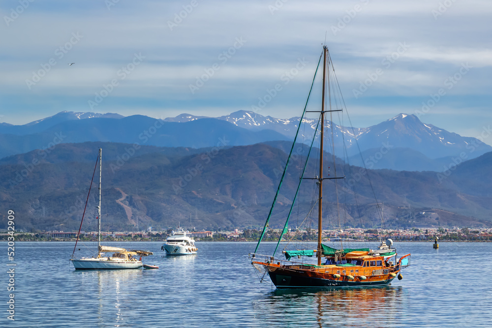 Sailing yachts are anchored against the background of small town houses, mountains and blue sky