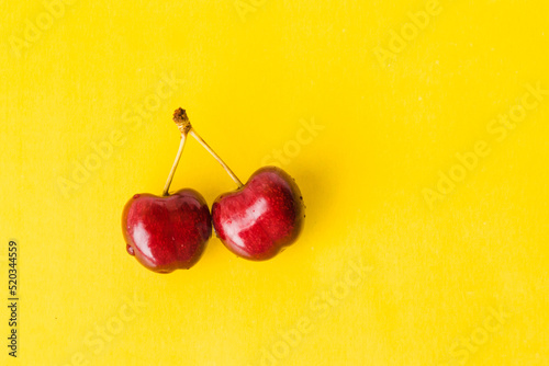 Two juicy berries of a red cherry on a yellow background. Couple of red juicy cherries with stems