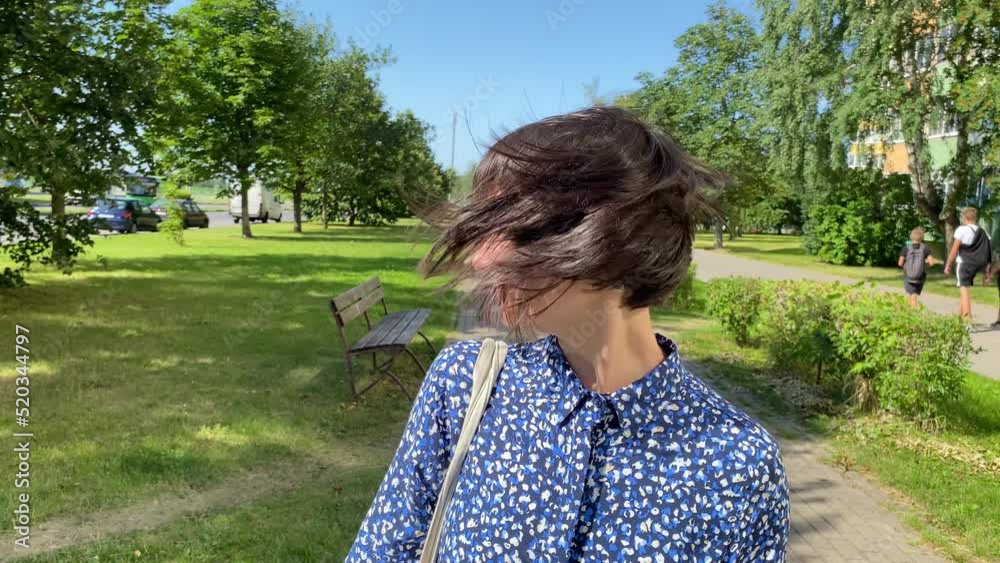Young Caucasian brunette woman is swinging joyfully her hair. Pretty girl with short-medium bob hairstyle outdoors