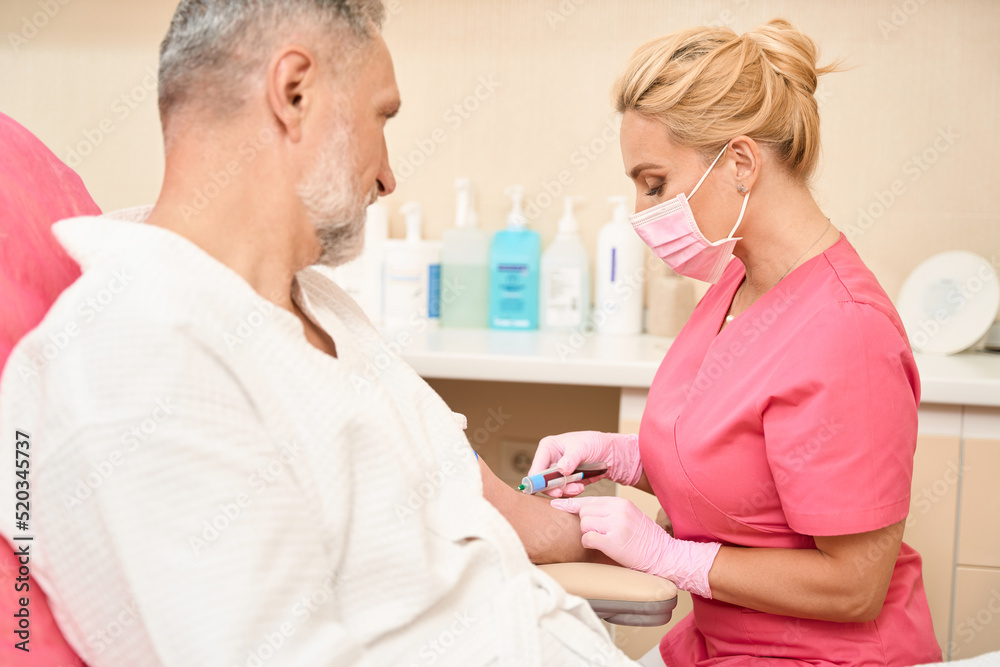 Fototapeta premium Beautiful nurse taking blood sample from man in doctor's office