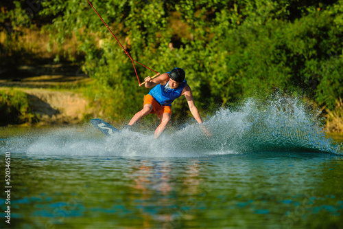 Fototapeta Naklejka Na Ścianę i Meble -  A professional wakeboarder rides on the lake in sunny weather, performing figures