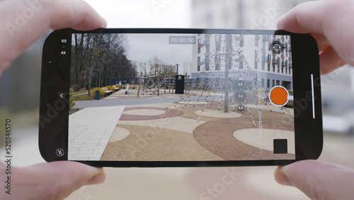 Close-up of screen of phone taking video. Action. Man holds phone and takes video of playground and multi-storey building