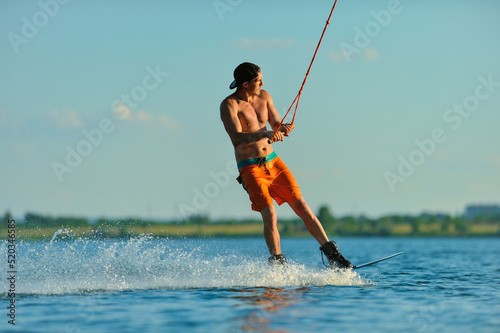 A professional wakeboarder rides on the lake in sunny weather, performing figures