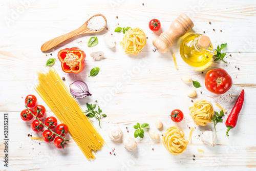 Italian food background on white kitchen table. Food frame. Raw Pasta, olive oil, spices, tomatoes and basil. Top view with copy space.