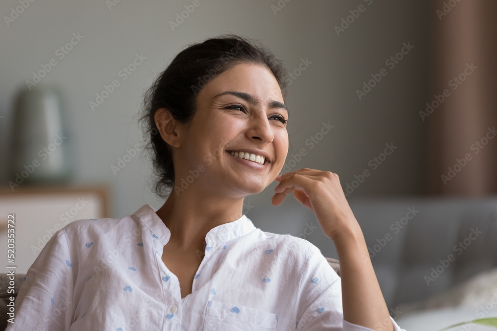 Happy beautiful young Indian woman looking at window with toothy smile, thinking of future vision, good news, dreaming, touching chin, facial skin, laughing. Head shot portrait Happy beautiful young Indian woman looking at window with toothy smile, thinking of future vision, good news, dreaming, touching chin, facial skin, laughing. Head shot portrait
