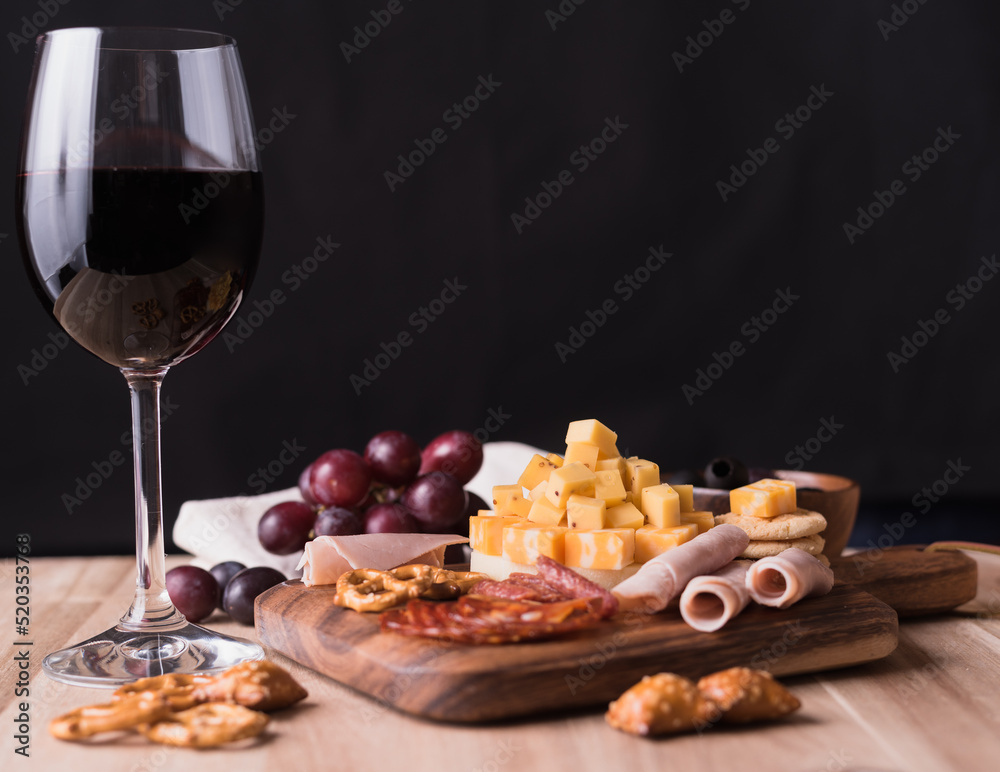 Cheese platter with organic cheeses, snacks, grapes, sliced of ham and wine on wooden background.