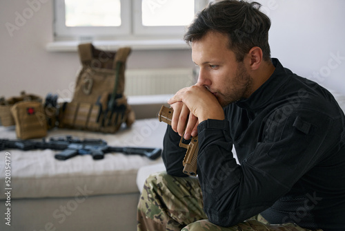 Fototapeta Military man with handgun having a seat in flat
