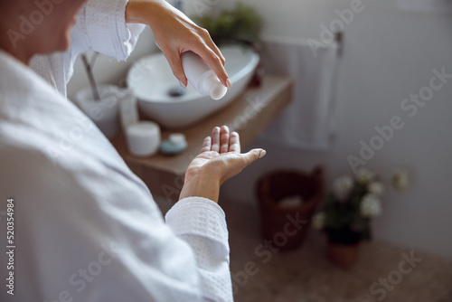 Close up of Caucasian female applying lotion on hand for moisturizing in bathroom.