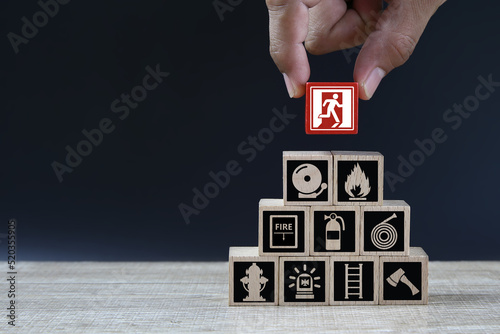 Fototapet Hand choose cube wooden toy block stack with door exit sing or fire escape with fire prevent icon and fire extinguisher and emergency prevention or protection symbol for safety and rescue