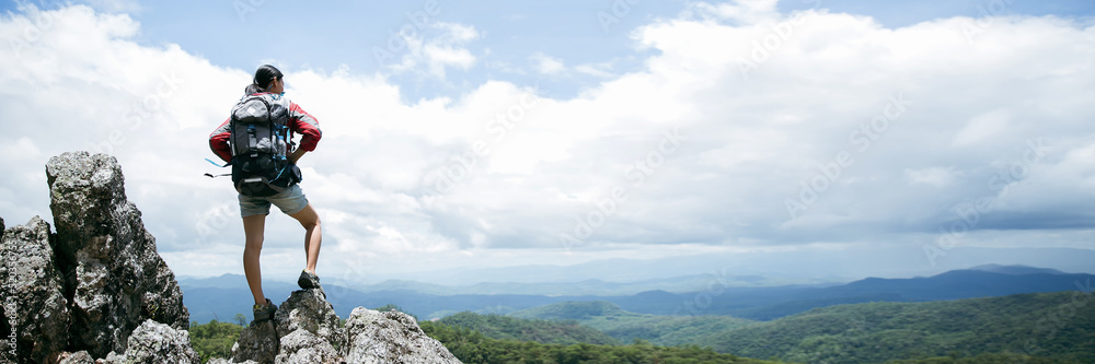 Young person hiking female standing on top rock, Backpack woman looking at beautiful mountain in summer, Landscape with sport girl, panorama hills, forest. Travel and tourism. banner with copy space