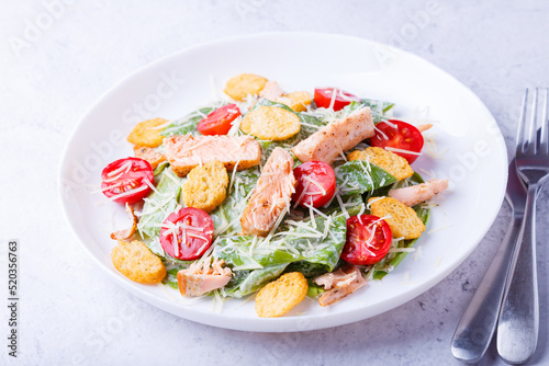 Caesar salad with red fish (salmon, trout), cherry tomatoes, croutons, parmesan cheese and romaine. Traditional American dish. Close-up, selective focus.