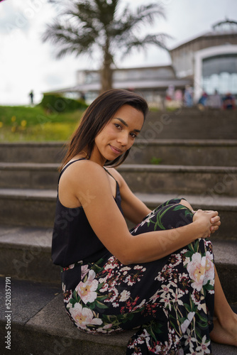 posing on a bleachers a young brunette woman with short straight hair, wears a flower print skirt, lifestyle, natural beauty and fashion