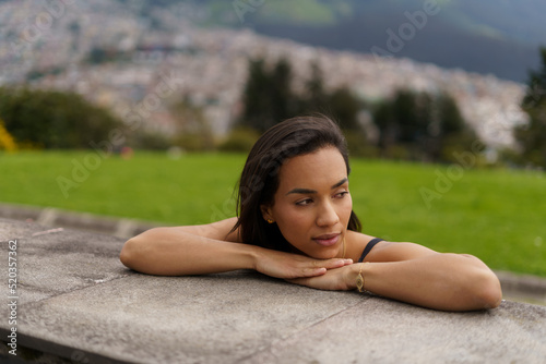 young Latin brunette woman with short hair leaning against a platform worried  mountain and city background  beauty and emotions