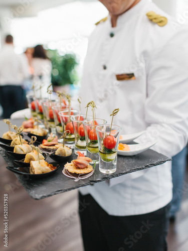 Obraz na plátně The waiter holds the appetizers on a black slate stand—pancakes with red caviar, Caprese in a glass on skewers