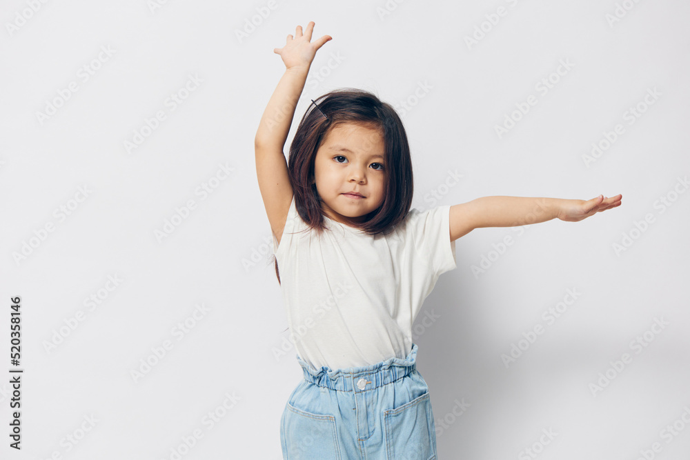 a cute, cheerful preschool girl stands happily raising her hands up on a light background with an empty space for inserting an advertising layout a cute, cheerful preschool girl stands happily raising her hands up on a light background with an empty space for inserting an advertising layout