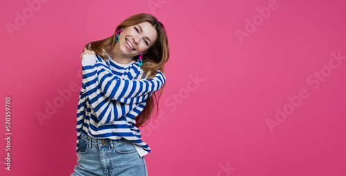 Happy young woman hugging self and smiling while standing against colored background
