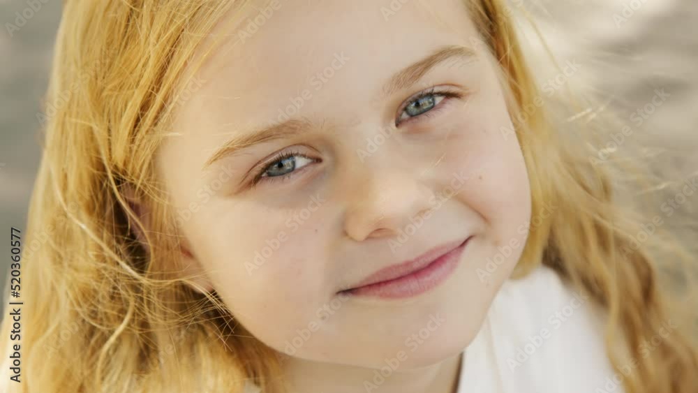 Portrait of a little girl looking at the camera, standing on the street in the city on a summer day. Young sad thinking curious child looking at camera closeup outdoors. Face Eyes Portrait of a little girl looking at the camera, standing on the street in the city on a summer day. Young sad thinking curious child looking at camera closeup outdoors. Face Eyes