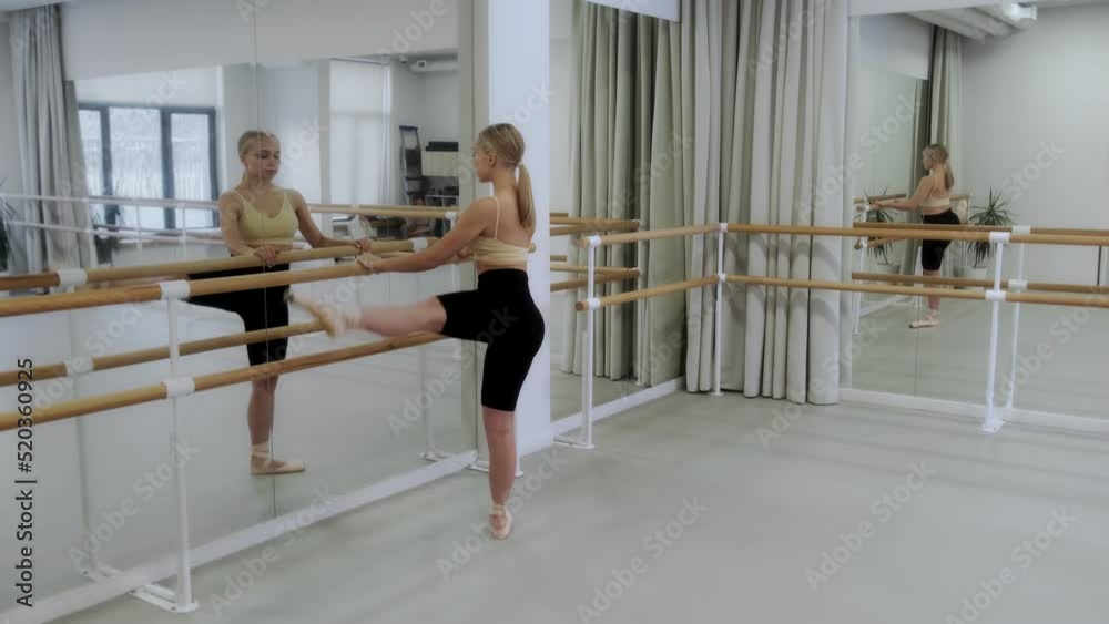 Ballerina rehearsing in the studio in front of a mirror at the white bright dance hall, ballet rehearsal, ballerina in the ballet studio, dance hall lesson, stretching and pilates, 4k. Ballerina rehearsing in the studio in front of a mirror at the white bright dance hall, ballet rehearsal, ballerina in the ballet studio, dance hall lesson, stretching and pilates, 4k.