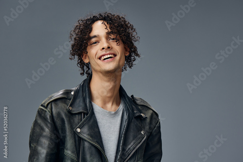 Cheerful smiling stylish tanned curly man leather jacket posing isolated on over gray studio background. Cool fashion offer. Huge Seasonal Sale New Collection concept. Copy space for ad