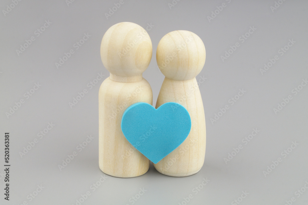 Female and male wooden figures with blue heart sticker on gray background. Female and male wooden figures with blue heart sticker on gray background.