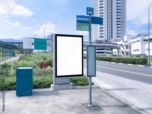 Photography Blank vertical advertising poster banner mockup at empty bus stop shelter by main road, greenery behind; out-of-home OOH vertical billboard media display space