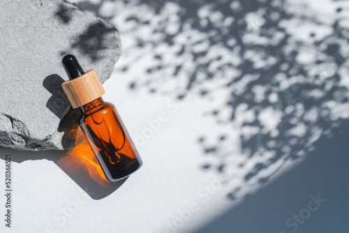 Amber dropper bottles with serum, tonic or essential oil on grey concrete podium. White background with daylight with flowers shadows. Beauty concept for face and body care