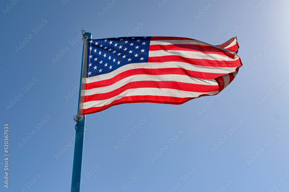 National American flag, the Stars and Stripes, backlit agianst a blue sky. No people. National American flag, the Stars and Stripes, backlit agianst a blue sky. No people.