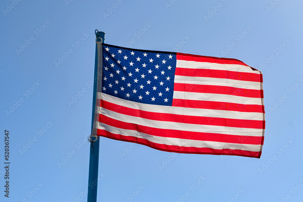 National American flag, the Stars and Stripes, backlit agianst a blue sky. No people.