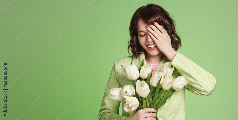 Romantic girl laughs, holds bouquet of fresh white tulips. Happy woman receives flowers and smiles, green background Romantic girl laughs, holds bouquet of fresh white tulips. Happy woman receives flowers and smiles, green background