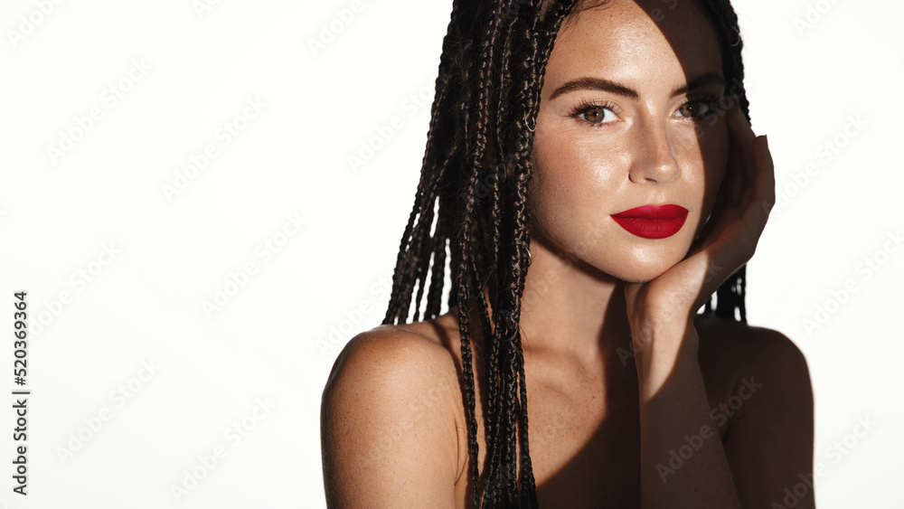 Beautiful woman with shade falling on her face, has red lipstick on, smiling sensual, gently touching her cheek, white background. Makeup concept Beautiful woman with shade falling on her face, has red lipstick on, smiling sensual, gently touching her cheek, white background. Makeup concept