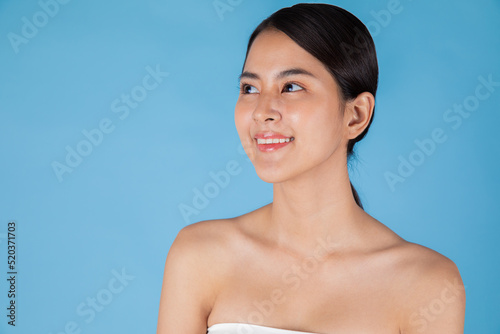 Smiling Asian woman touching healthy skin portrait. Beautiful happy girl model with fresh glowing hydrated facial skin and natural makeup on blue background at studio, Asian Skin care concept.