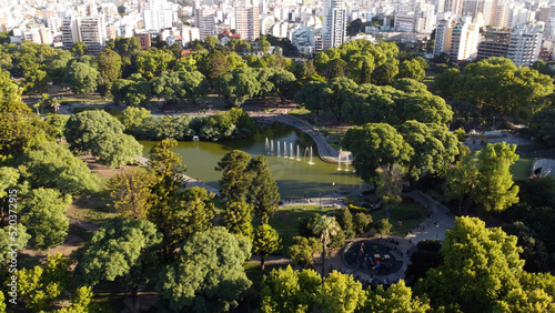 People having leisure time at Centenario green lush park lake with Buenos Aires city in background.