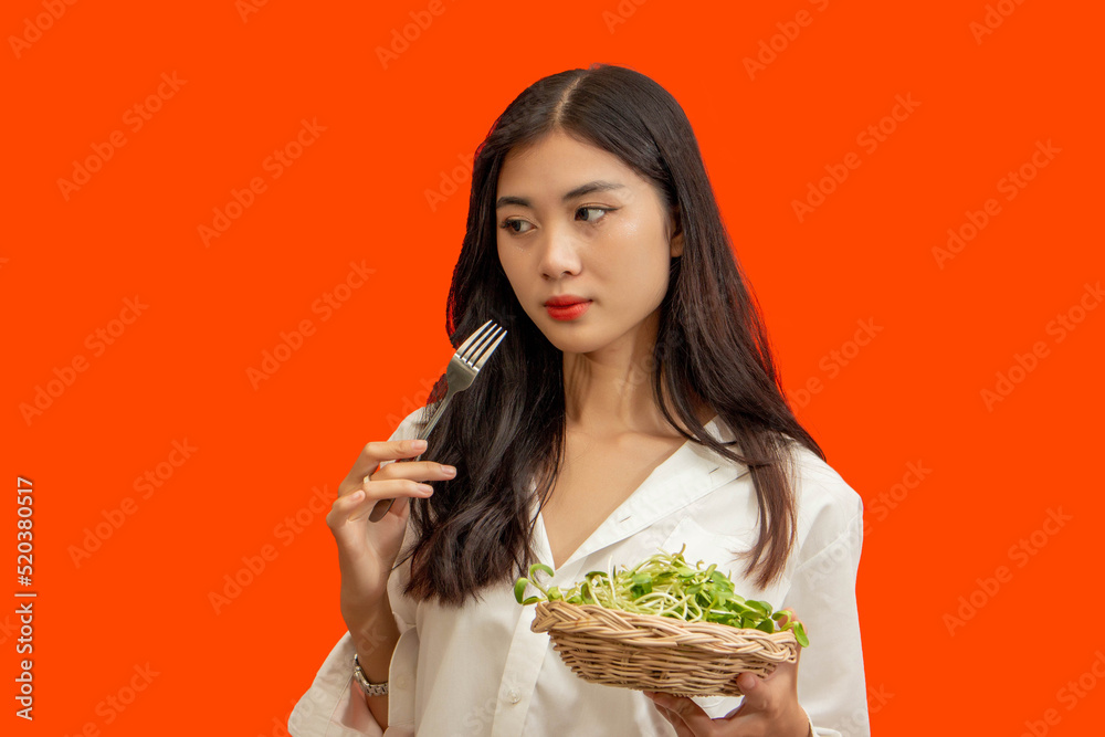 Vegetarian concept, Healthy woman eating sunflower sprouts standing isolated over orange background Vegetarian concept, Healthy woman eating sunflower sprouts standing isolated over orange background