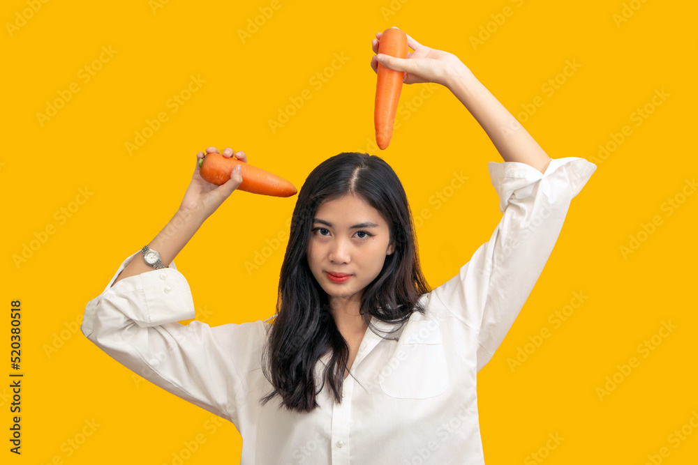 Vegetarian concept, Healthy woman in white shirt gesturing with carrot isolated yellow background