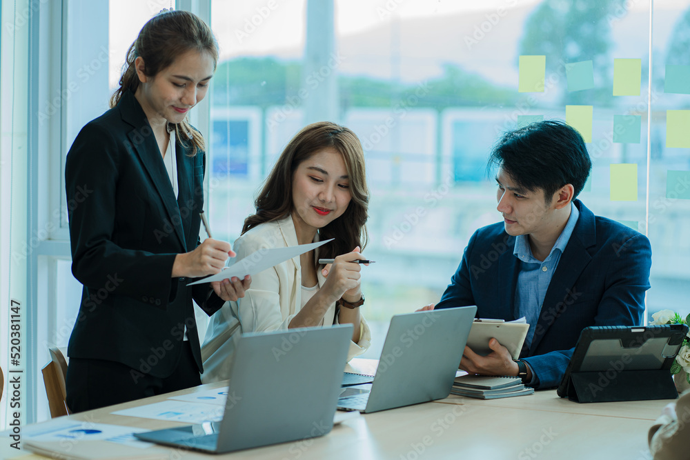 Young Asian business team working with laptops on financial documents with happy smiles. Group of business people meeting in a modern office Design and Concept Planning