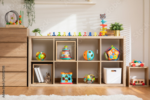 Interior of baby or child room with toys in cozy and warmth home. Nursery room with colorful toys in wooden box for development baby skill with morning light. Comfortable living room for kid and baby