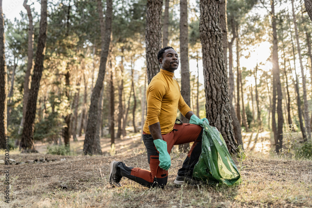Fototapeta premium African man, altruistic volunteer who collects garbage from the forest to protect the environment.